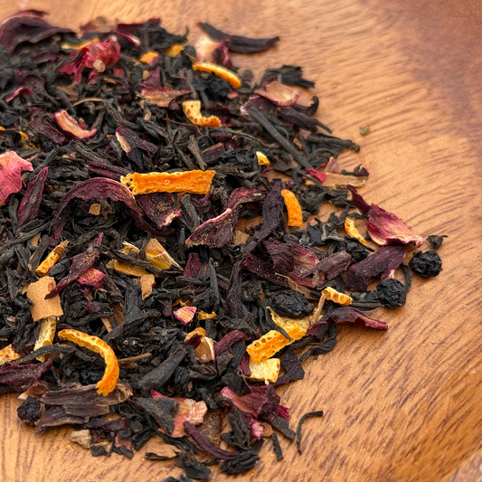 Dry black tea leaves with orange peel and other spices on a wooden surface